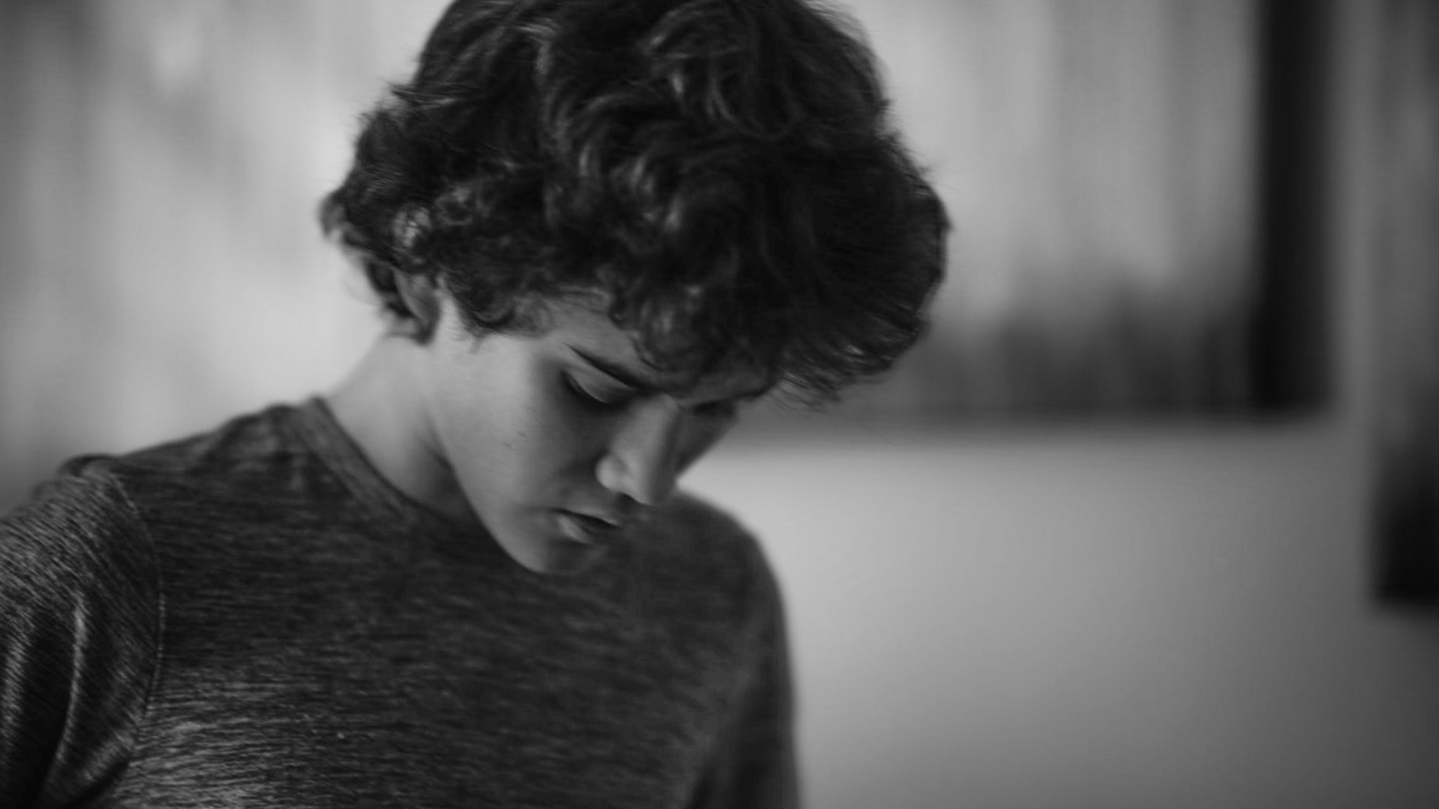 A child with curly hair looks down, quiet and absorbed, in a softly lit room.